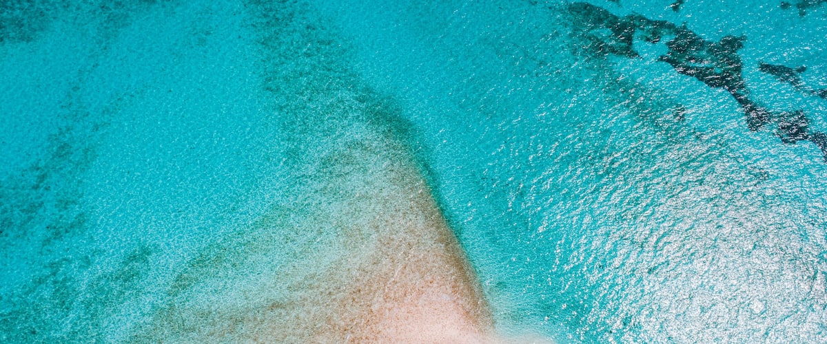 A clear turquoise sea with a sandy beach and a boat.
