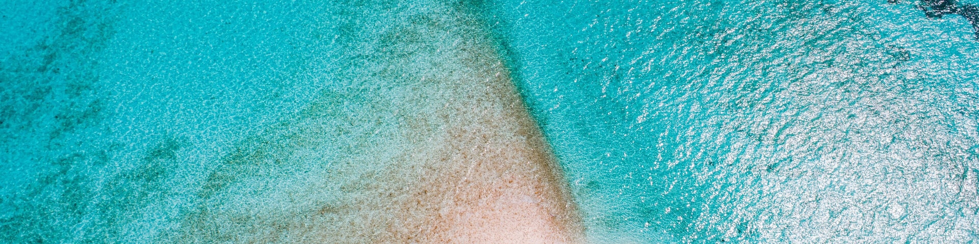 A clear turquoise sea with a sandy beach and a boat.
