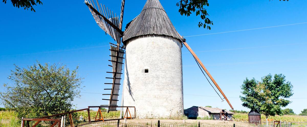 A traditional windmill with a conical roof, surrounded by trees and a fence.