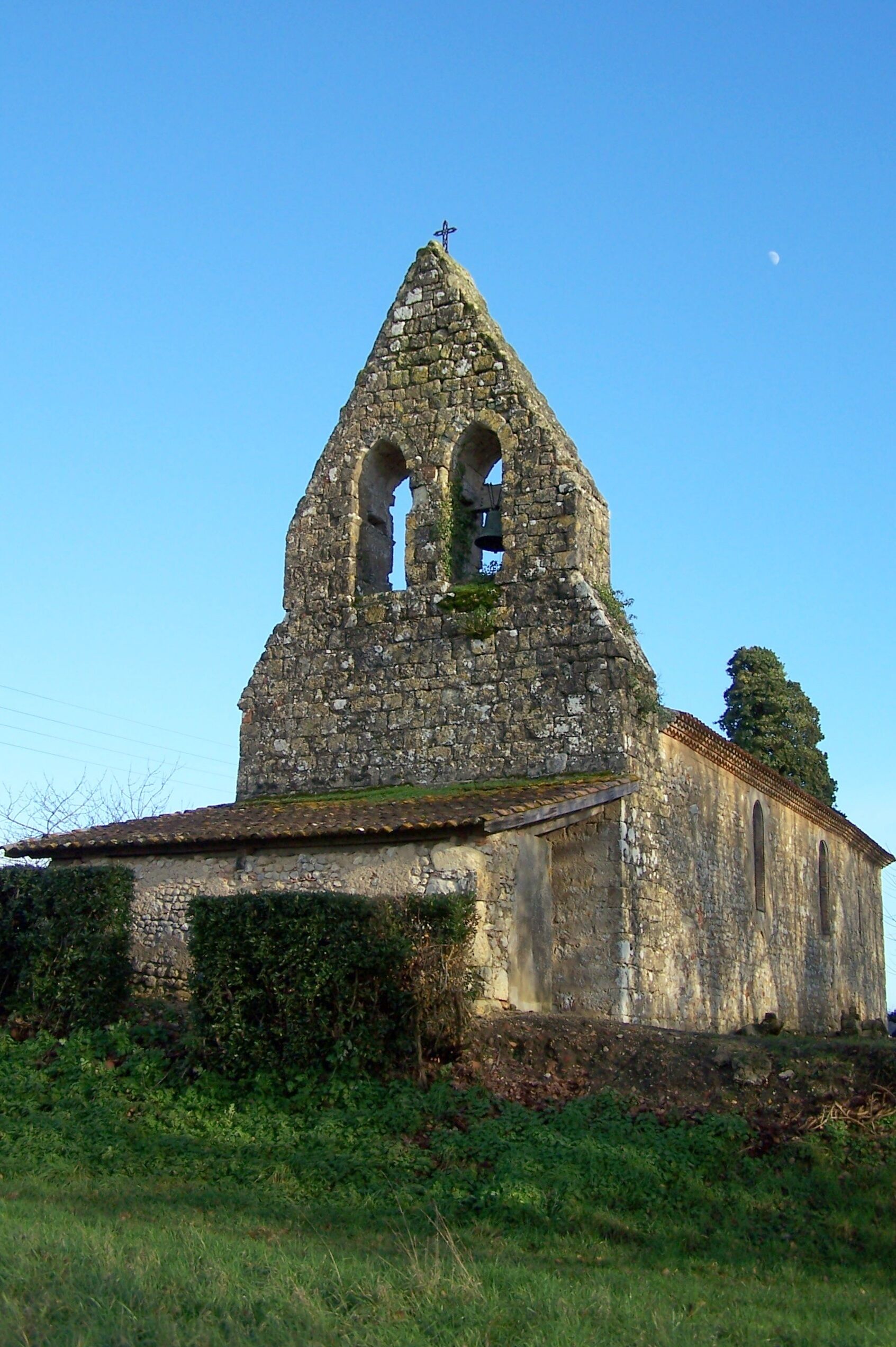 An old stone church with a bell tower, surrounded by greenery.