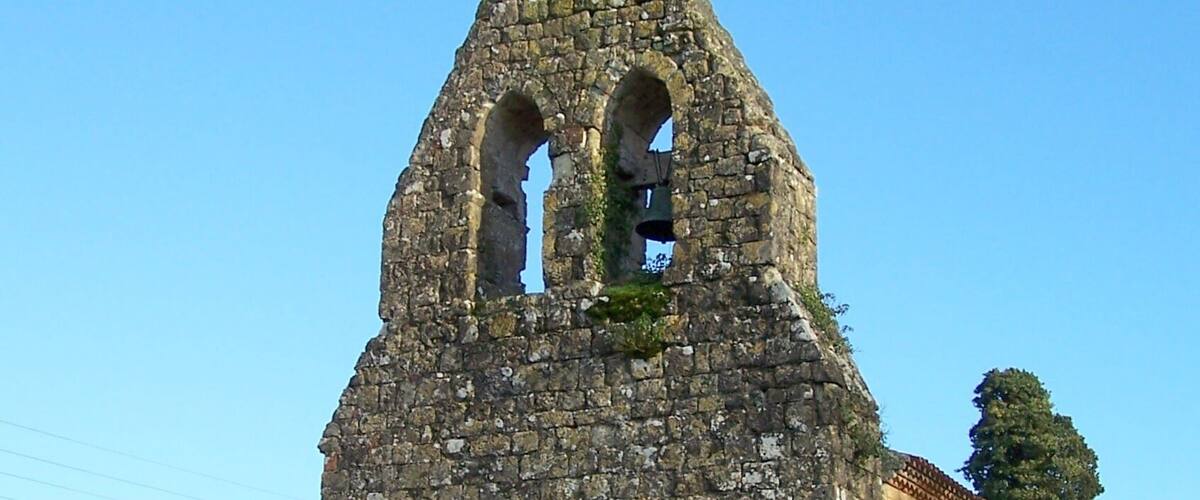 An old stone church with a bell tower, surrounded by greenery.
