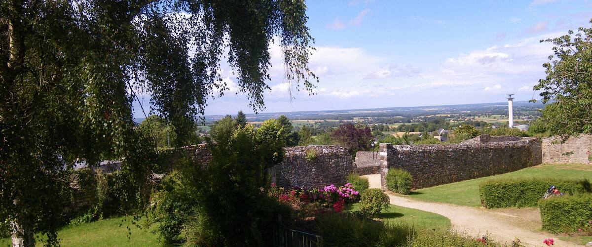 A historic stone wall, lush greenery, and a distant view of a tower.