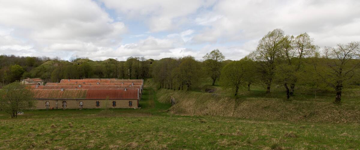A large brick building with a red roof, surrounded by green fields and trees.