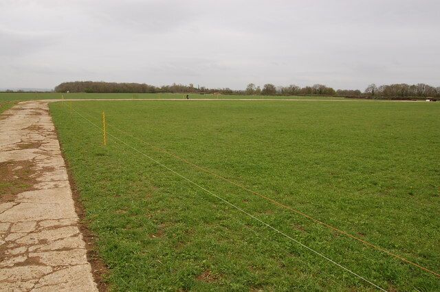 A large open field with a dirt path on the left and a fence running through the center.