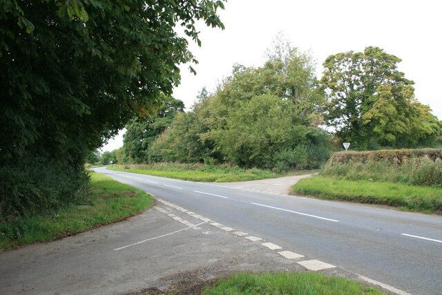 A rural road with a roundabout, surrounded by greenery and trees.