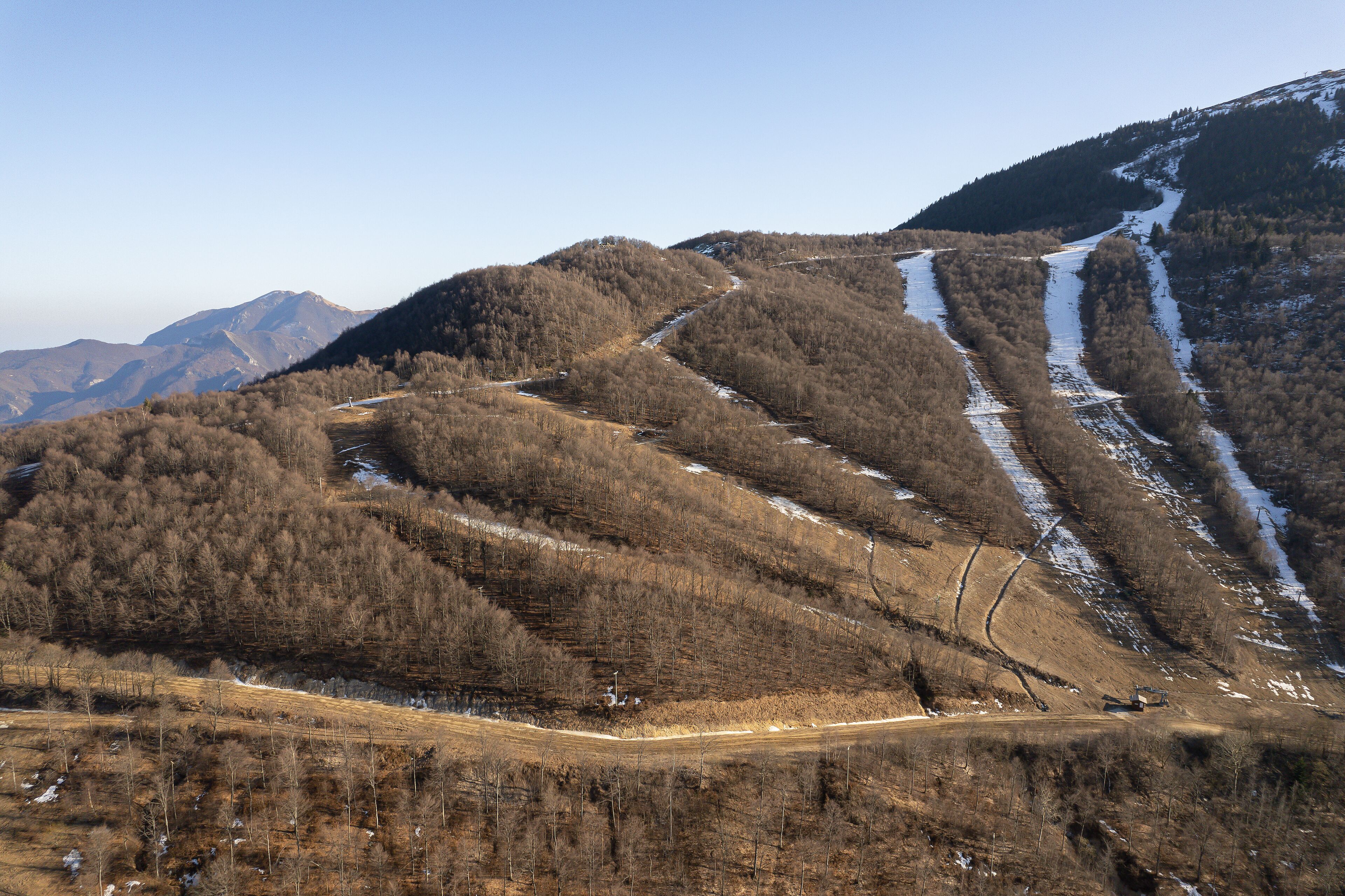 A mountainous landscape with a winding road, snow patches, and a clear sky.