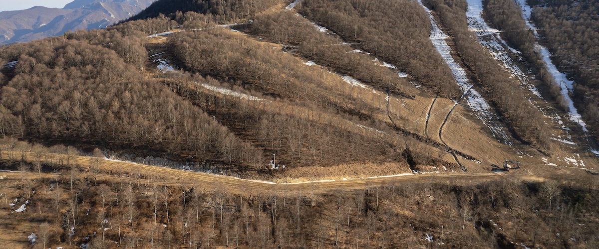 A mountainous landscape with a winding road, snow patches, and a clear sky.