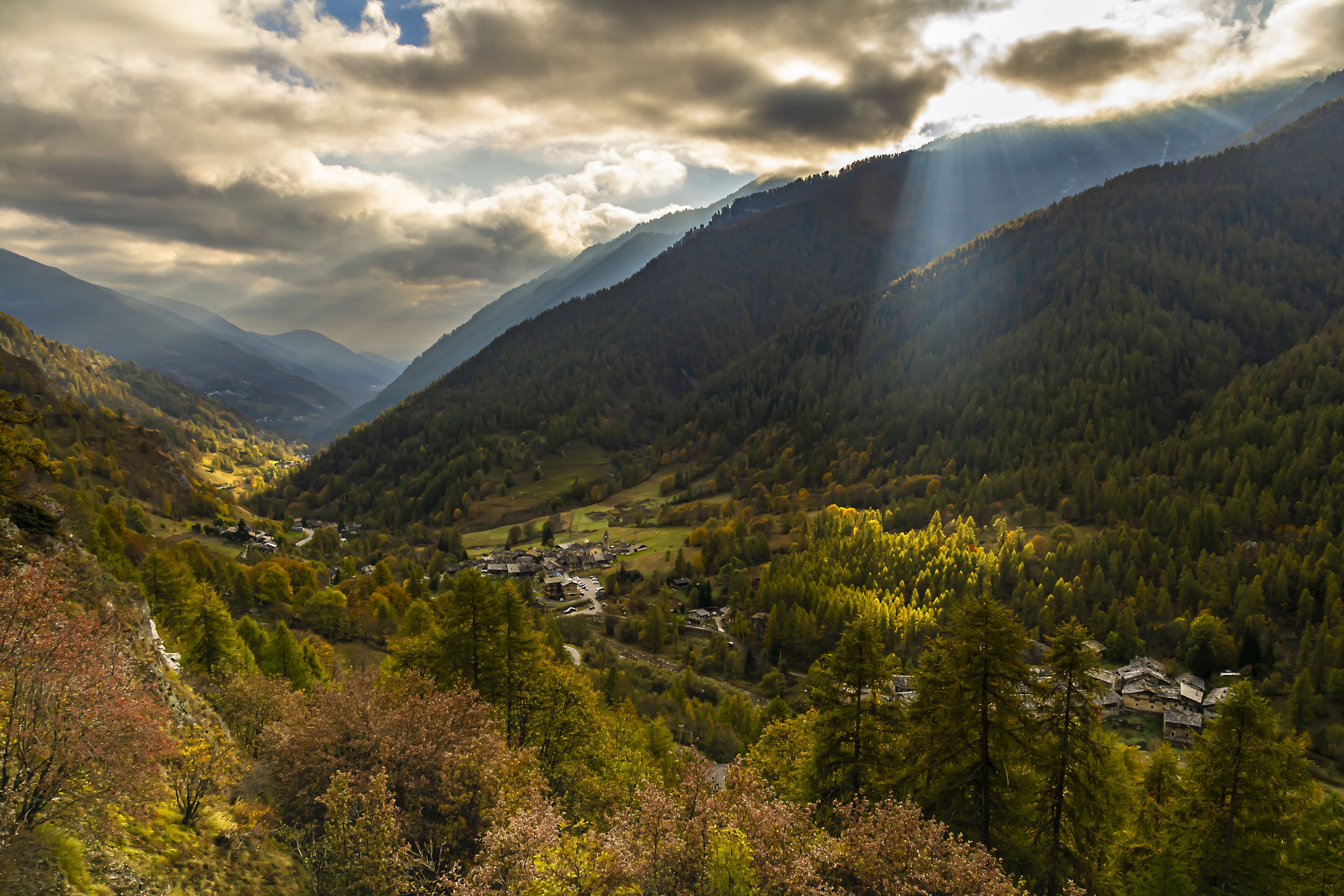 A valley with a small village surrounded by mountains and dense forests.