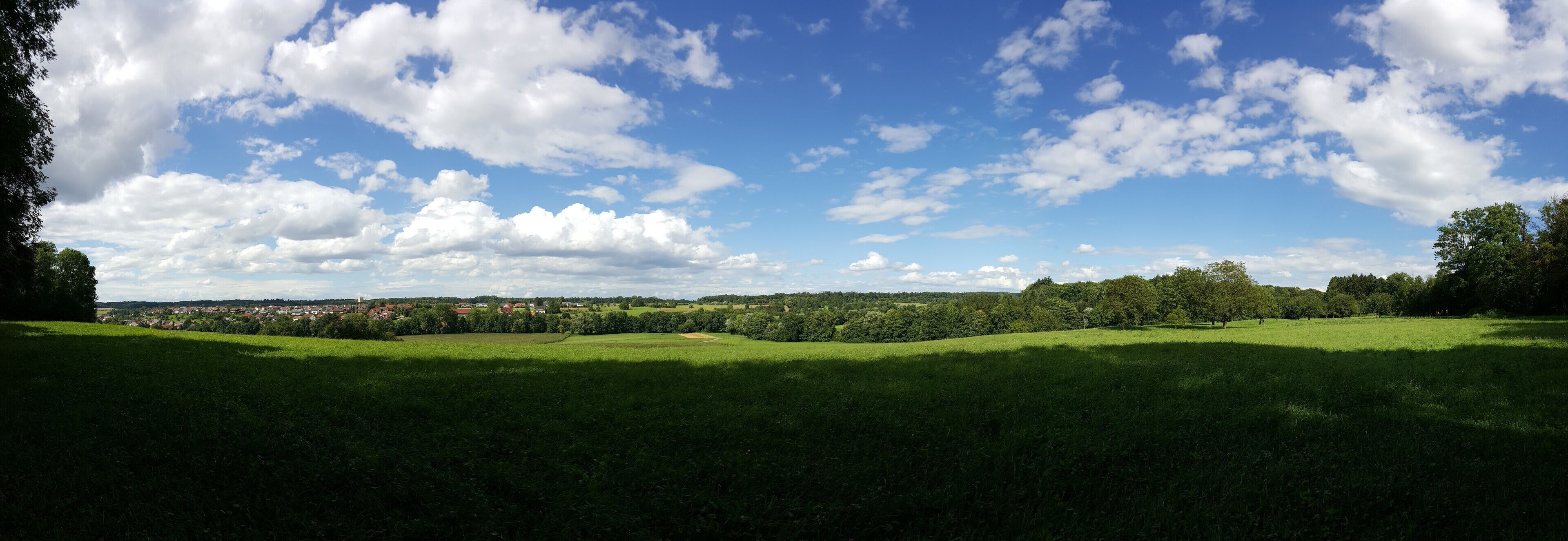 A green field with a town in the distance and a blue sky with clouds.