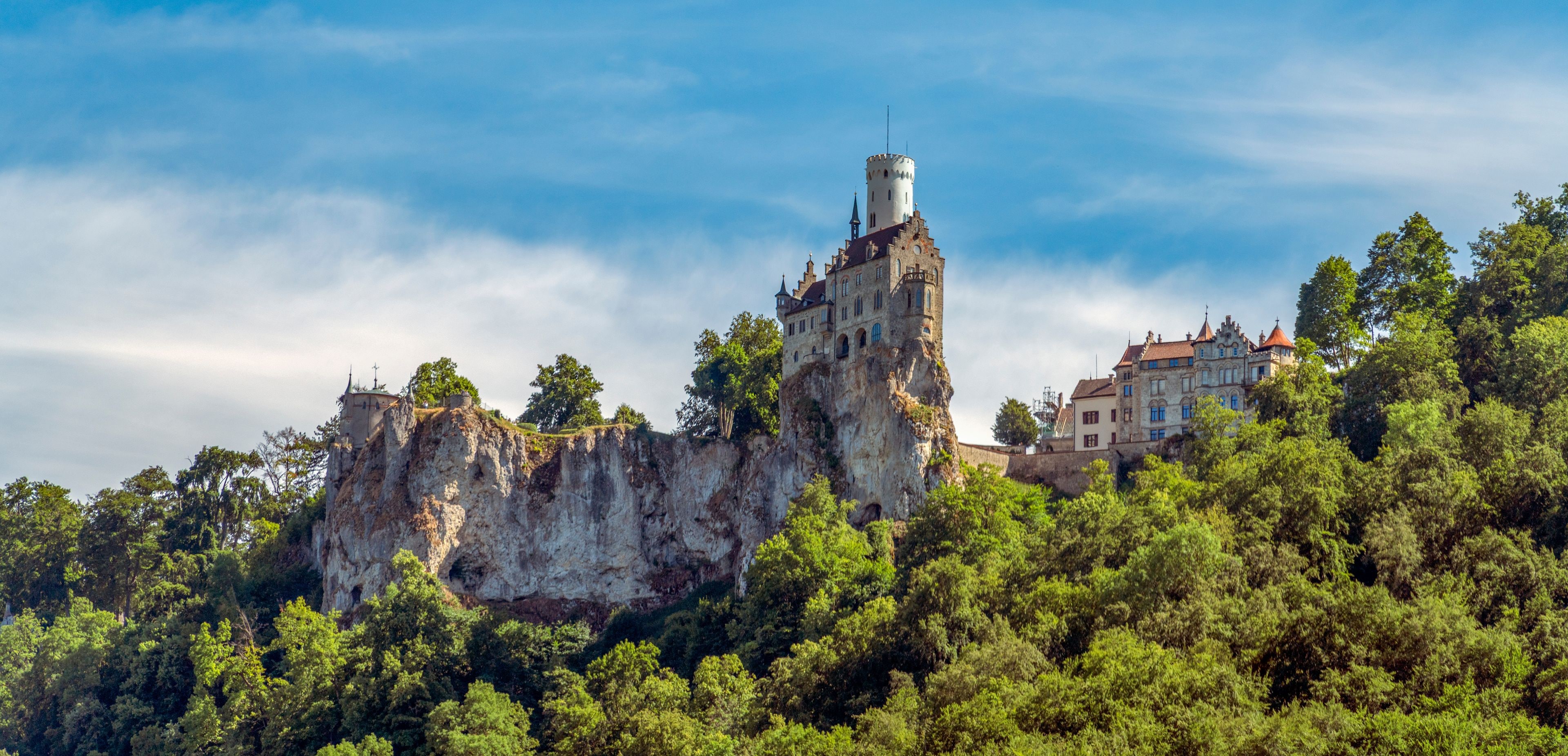 Eine Burg thront auf einem steilen Felsen, umgeben von dichtem Wald.