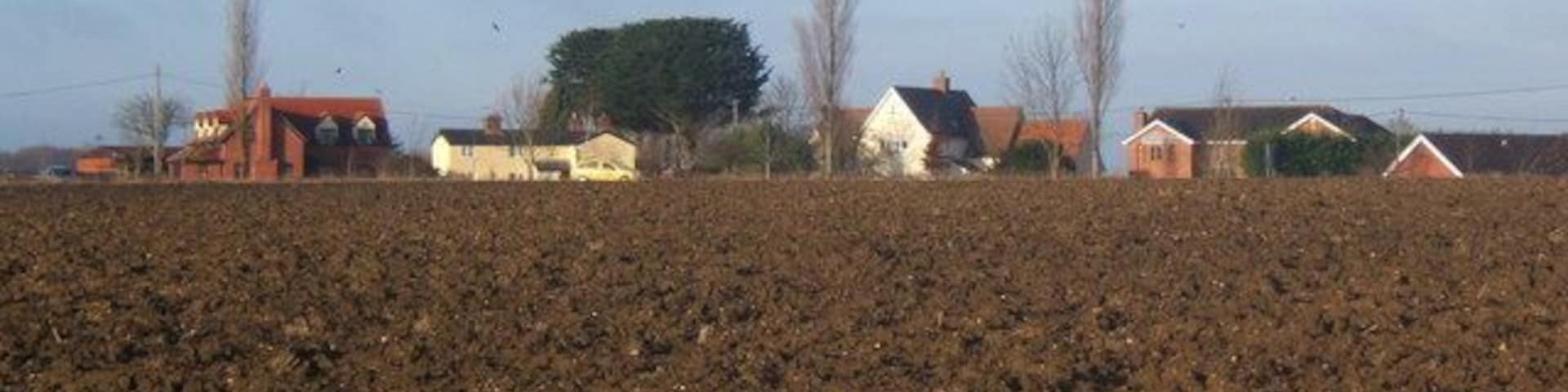 Ploughed field with Great Bricett beyond After recent wet weather the clay soil clung to the boots in great lumps.