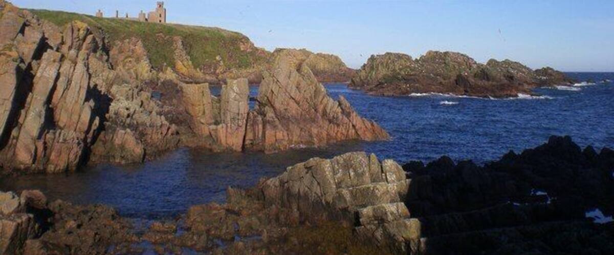 A coastal landscape with rocky cliffs, a small castle on a hill, and the ocean.