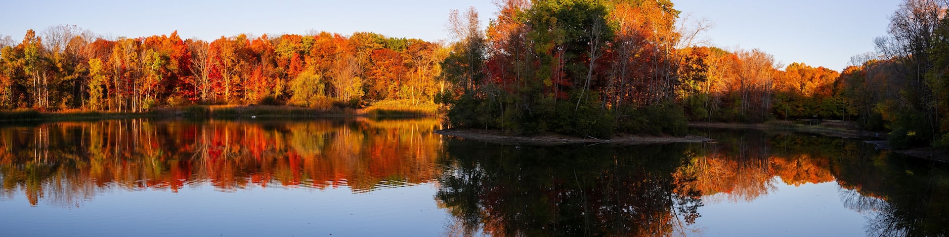 Panoramic view of island in scenic Maybury state park back lit trees with perfect reflection, Novi, Michigan