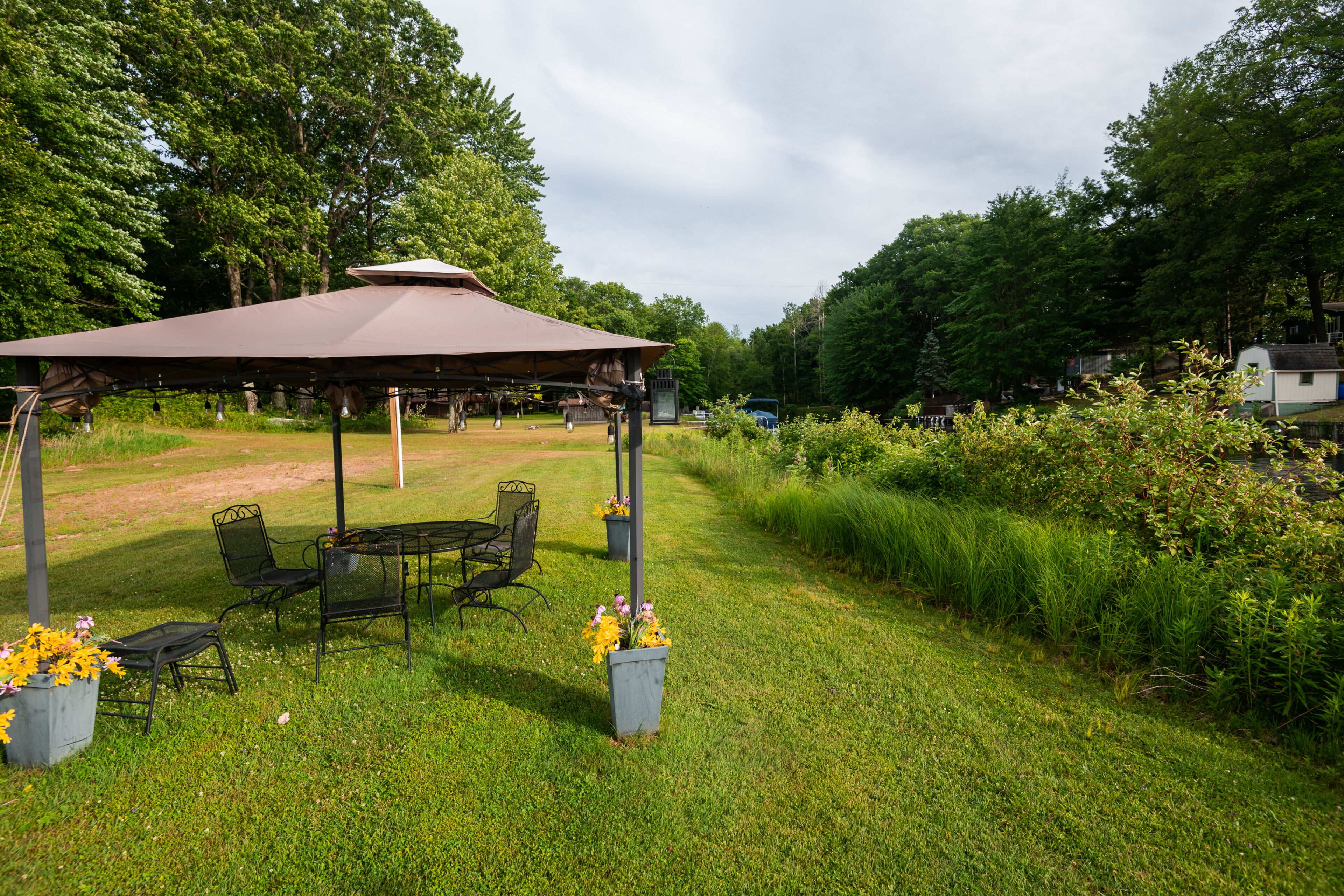 A gazebo with a table and chairs, surrounded by grass and flowers.