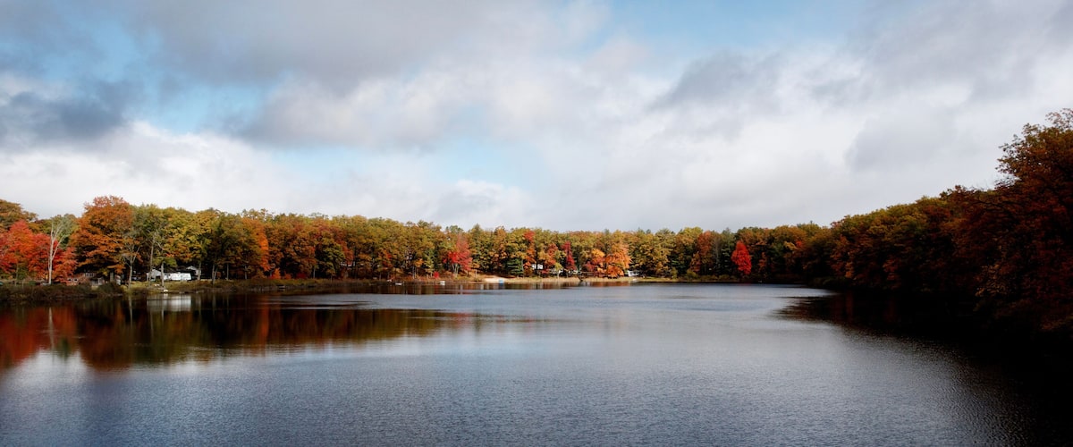 A calm lake surrounded by autumn-colored trees and a cloudy sky.