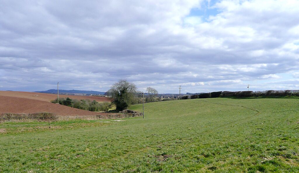 Farmland near Blakeshall, Worcestershire This is the wide angle view looking towards Cookley. The footpath across the field to Cookley via Debdale is clearly visible on the grass. The reddish colour of the soil is due to the Bunter sandstone rock and pebble beds of the area.