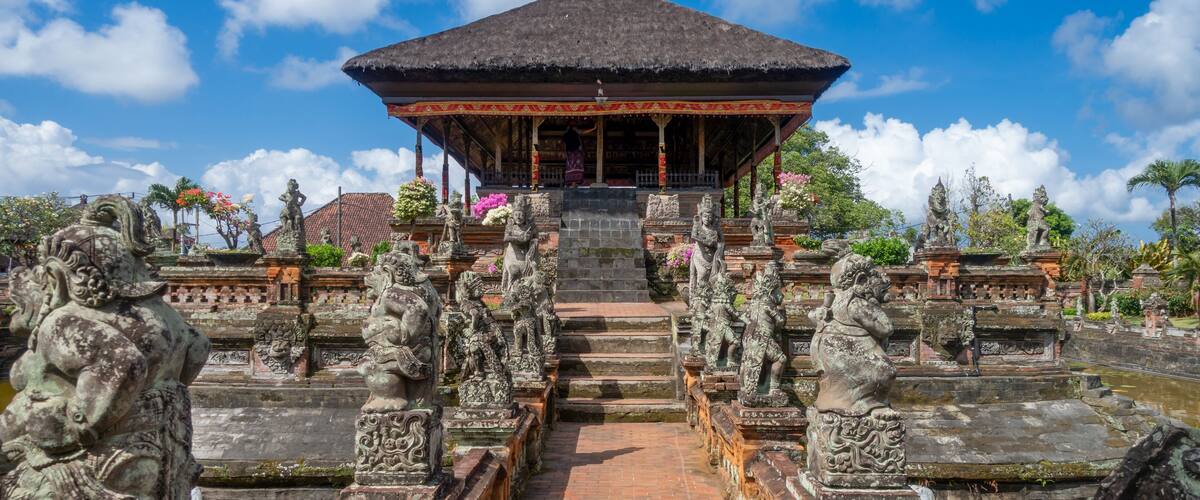 A temple with a thatched roof, statues, and a water channel.