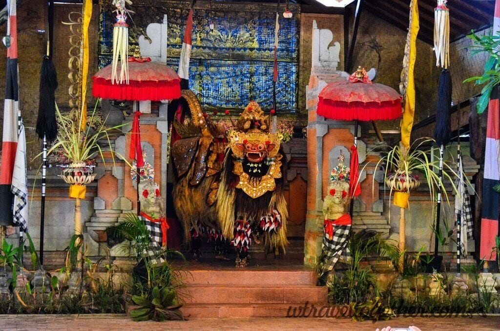 A traditional Balinese temple entrance with ornate decorations, a central deity statue, and a vibrant red umbrella.