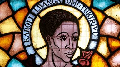 A stained glass window with a halo and the name "Karoli Lwanga Omukirivu".