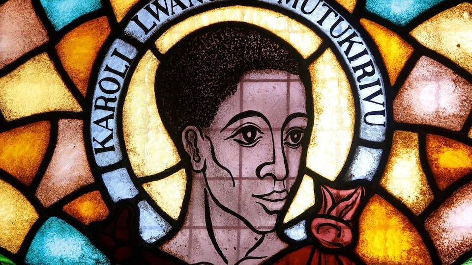 A stained glass window with a halo and the name "Karoli Lwanga Omukirivu".