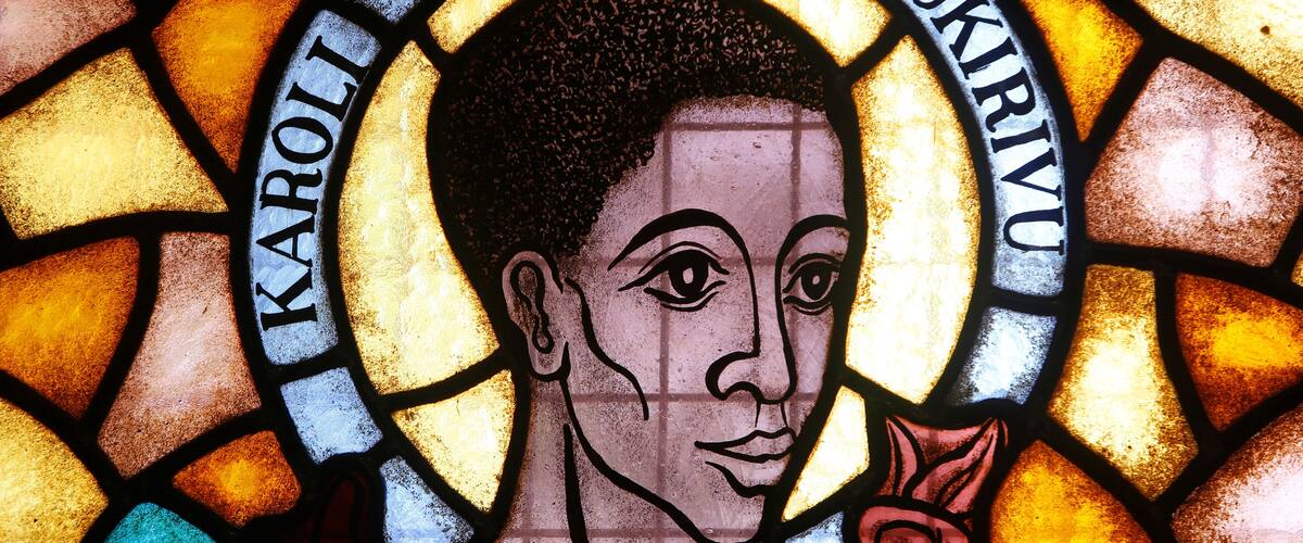 A stained glass window with a halo and the name "Karoli Lwanga Omukirivu".