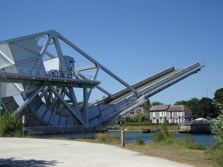A large metal bridge structure over a river with a house in the background.