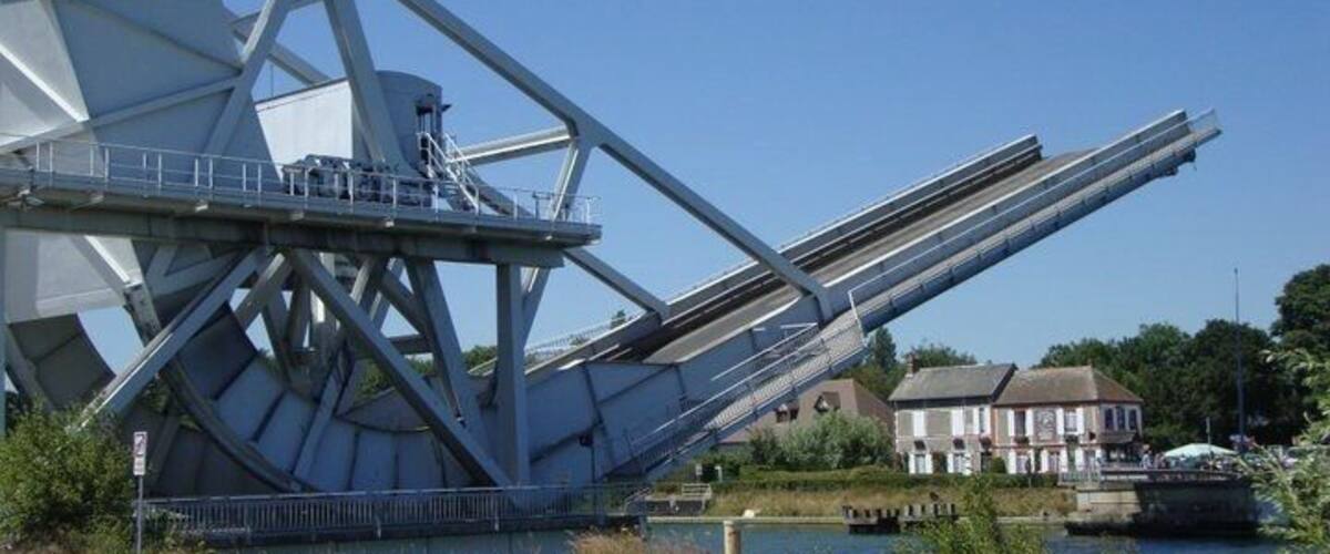 A large metal bridge structure over a river with a house in the background.