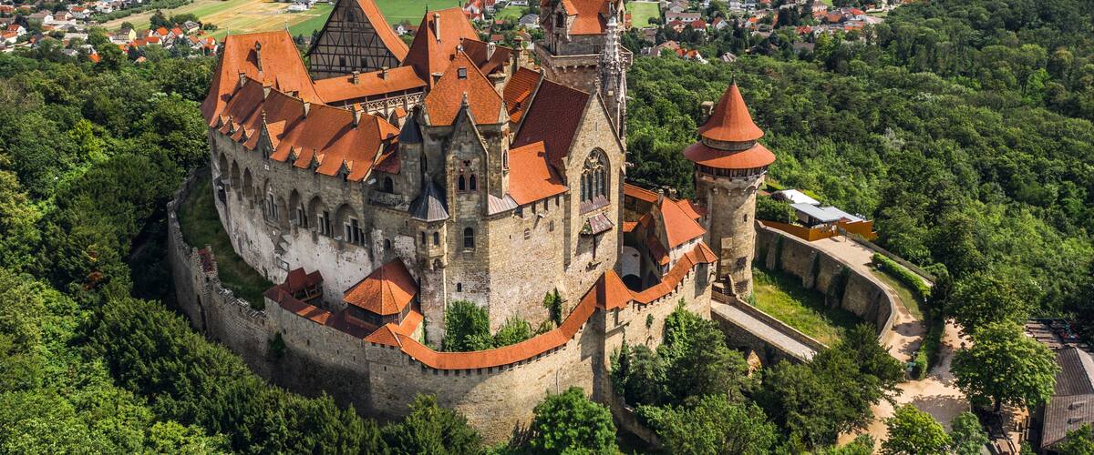A historic castle surrounded by lush greenery, with a view of the surrounding countryside and fields.