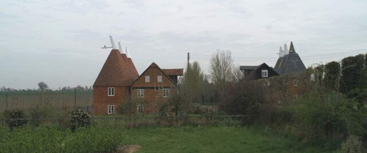 A rural landscape with a large brick house, a windmill, and a field.
