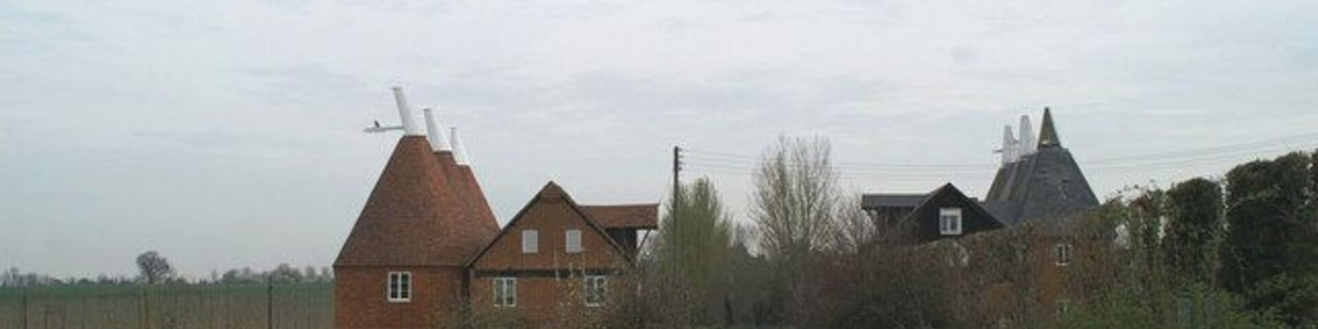A rural landscape with a large brick house, a windmill, and a field.