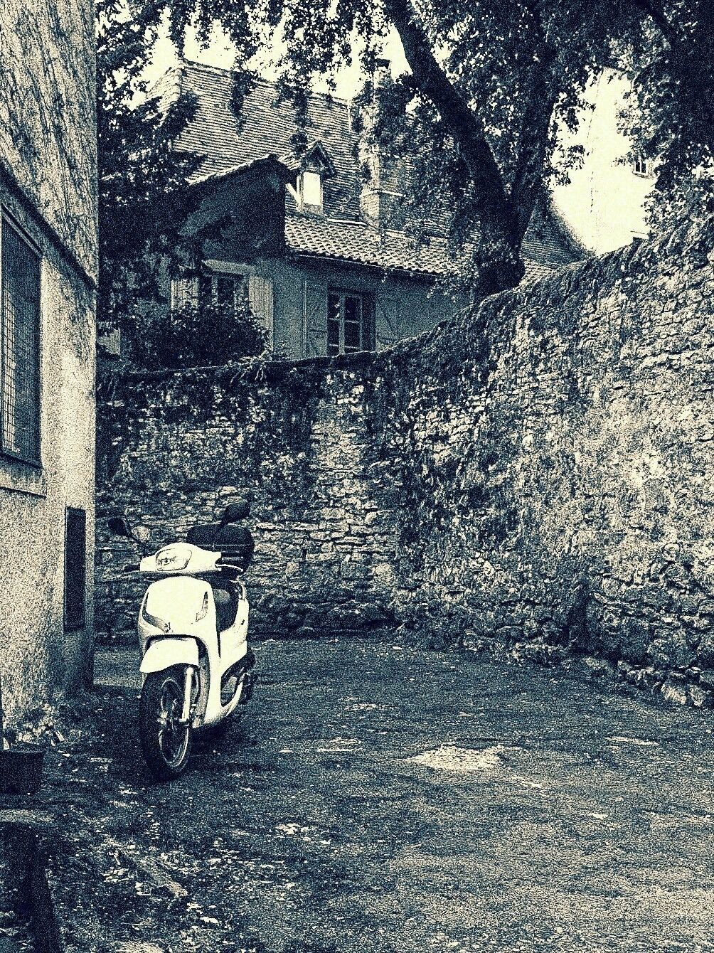 A scooter parked in front of a stone building with a tiled roof, surrounded by trees.