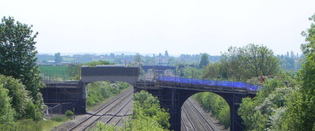 A railway bridge over tracks with greenery on either side.
