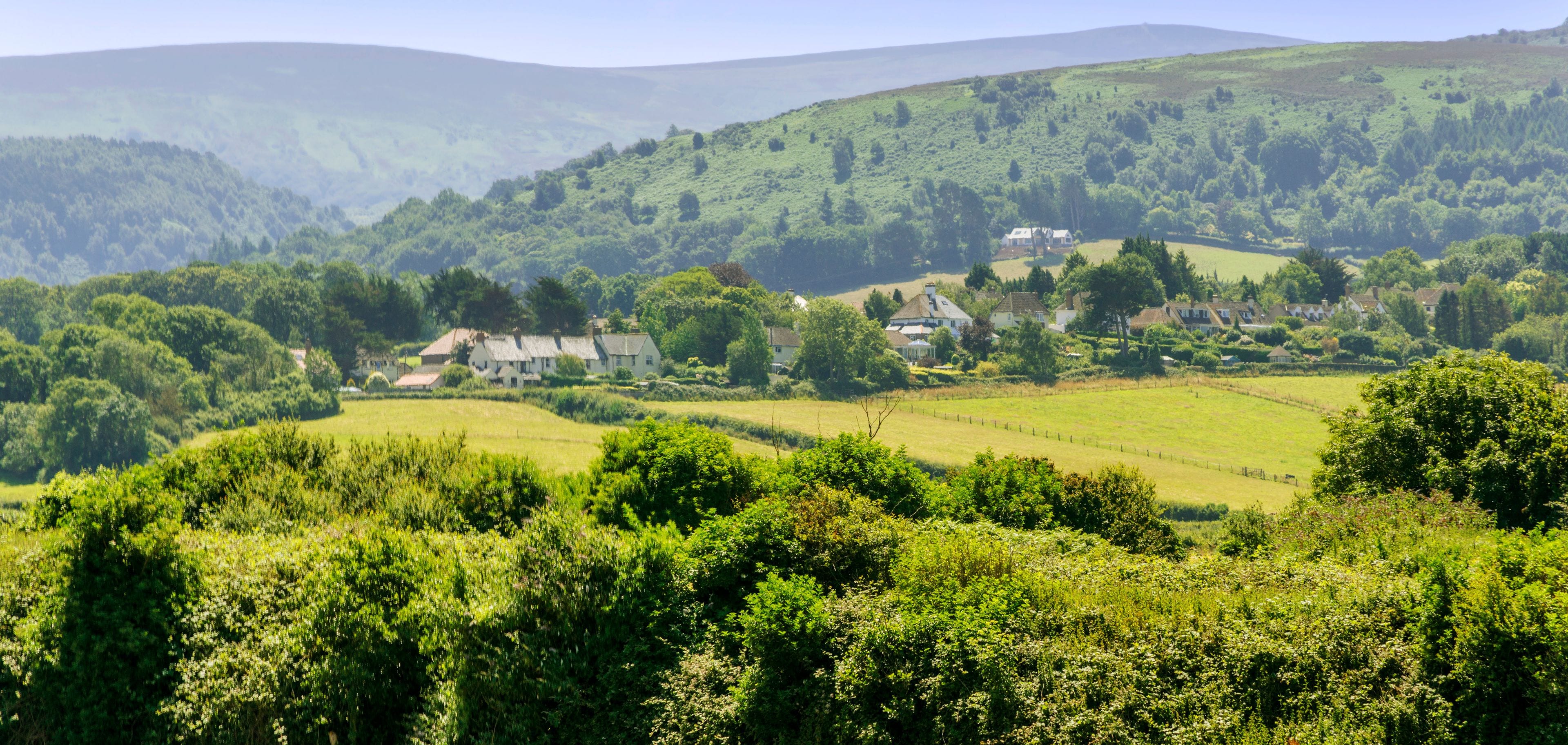 Rolling hills, lush greenery, and scattered houses in a rural landscape.