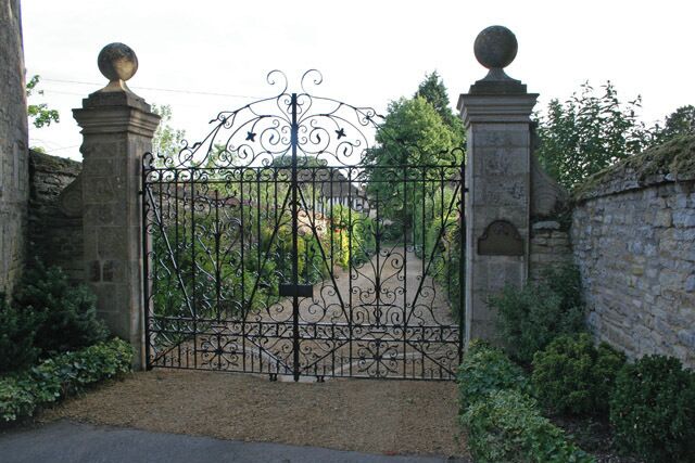 A wrought iron gate with decorative elements, flanked by stone pillars and a stone wall.