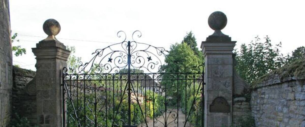 A wrought iron gate with decorative elements, flanked by stone pillars and a stone wall.