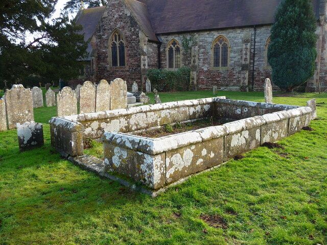 A church with a graveyard and a stone structure in the foreground.