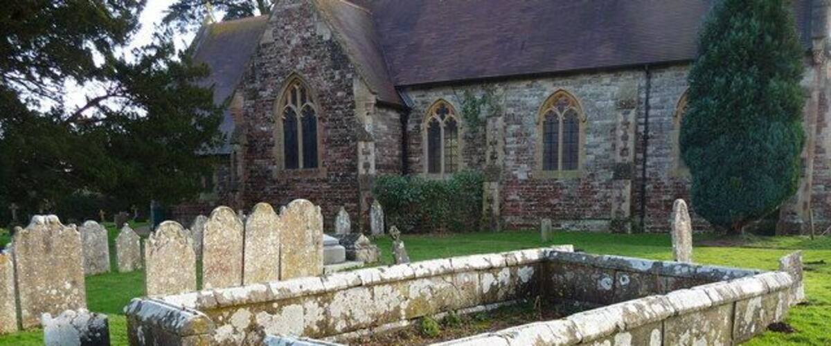 A church with a graveyard and a stone structure in the foreground.