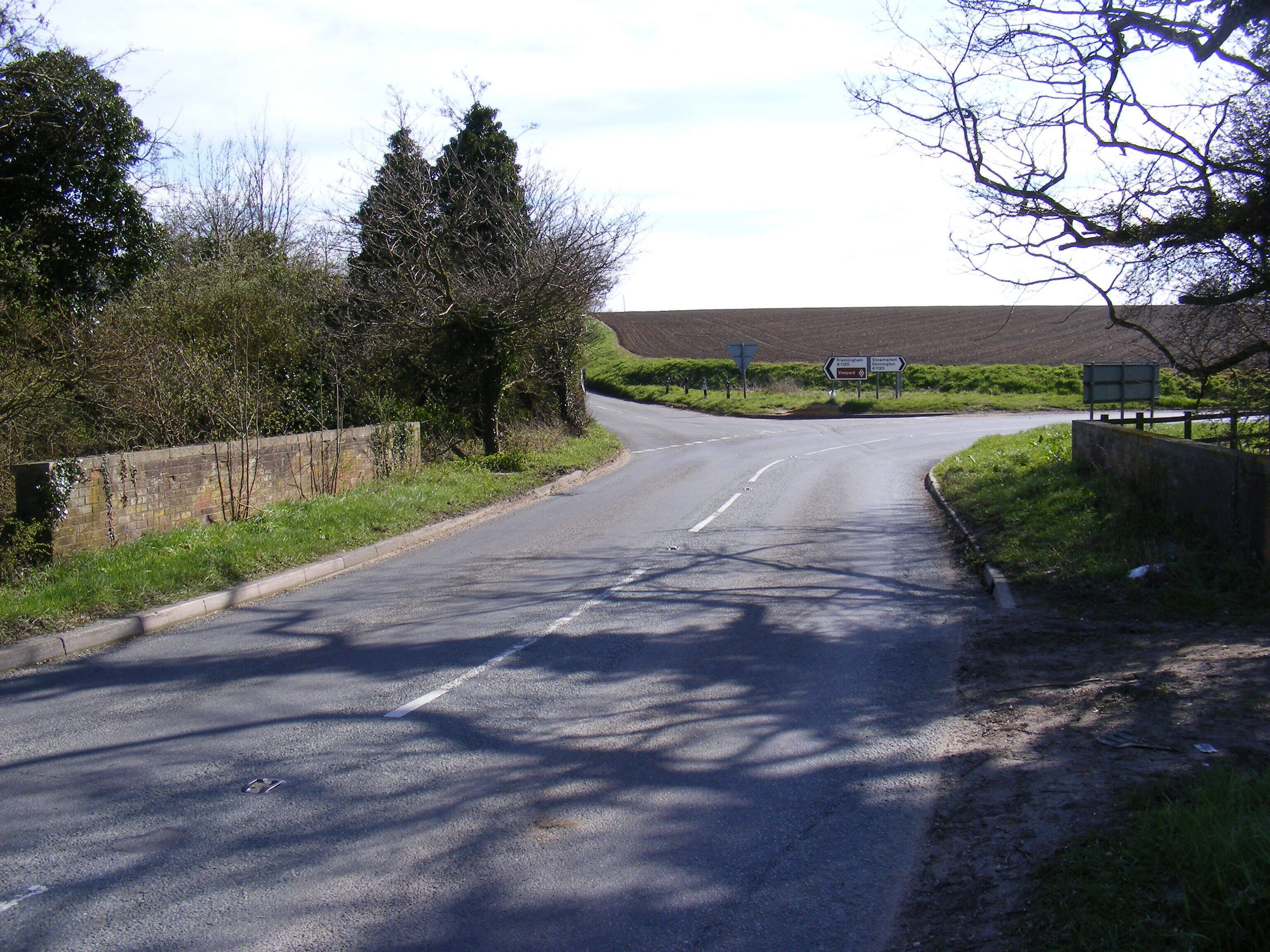 A rural road with directional signs, a stone wall, and trees.