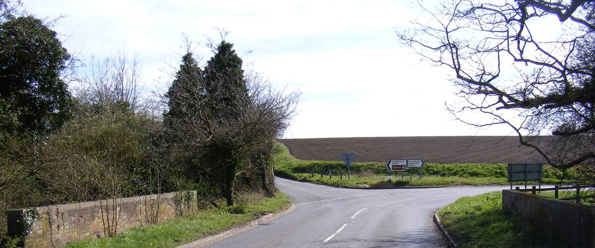 A rural road with directional signs, a stone wall, and trees.