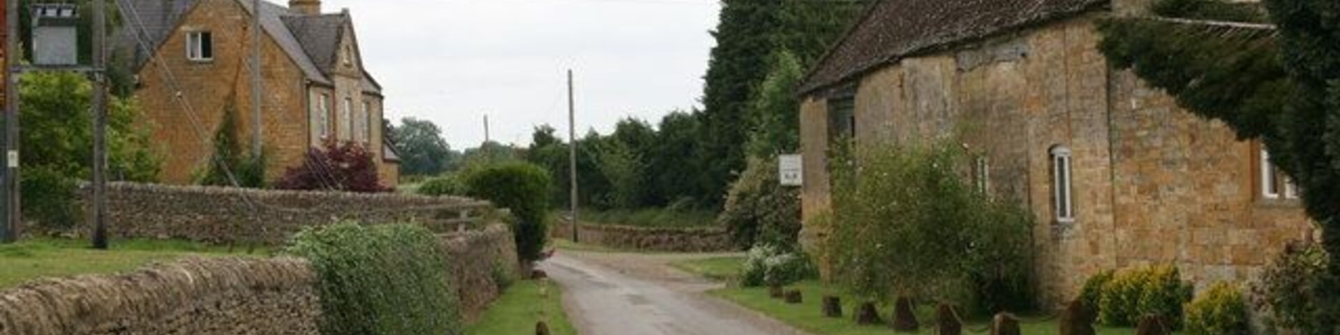 A rural road flanked by stone walls and houses, with a stone building on the right and a stone wall on the left.