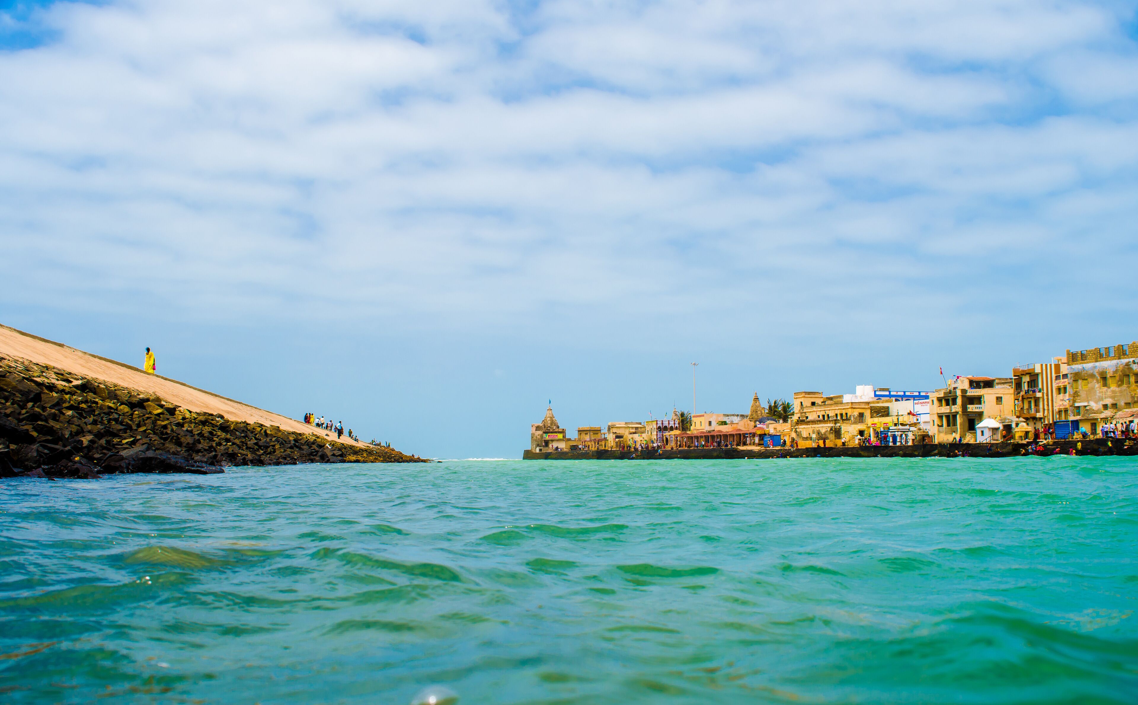 A coastal town with a rocky shoreline, clear turquoise waters, and a mix of traditional and modern buildings.