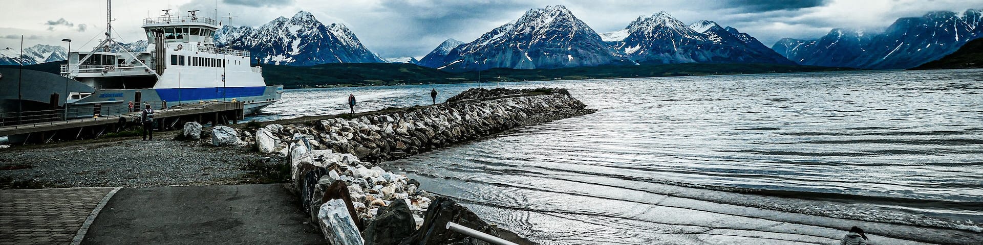 A boat docked at a pier with a rocky shoreline and mountains in the background.