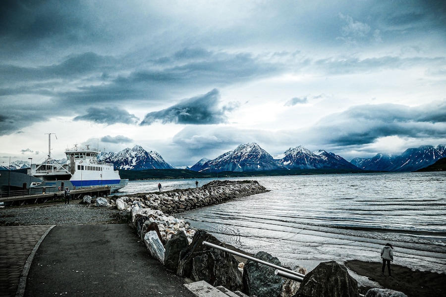 A boat docked at a pier with a rocky shoreline and mountains in the background.