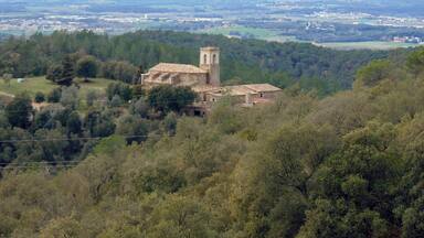 A historic church with a bell tower surrounded by lush greenery and mountains in the background.