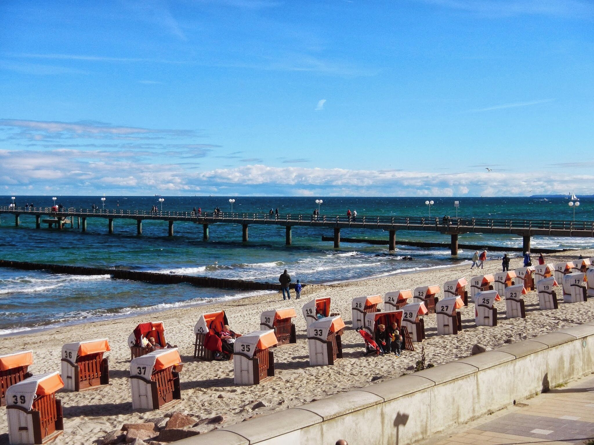 A beach with numbered beach huts and a pier extending into the water.