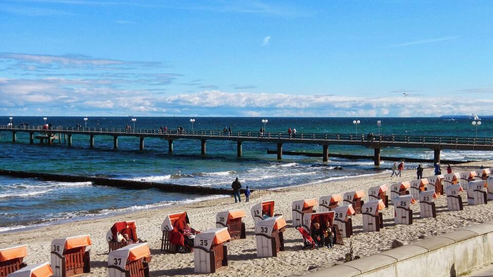 A beach with numbered beach huts and a pier extending into the water.