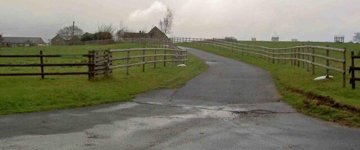A rural road with a wooden fence on one side and a grassy field on the other.