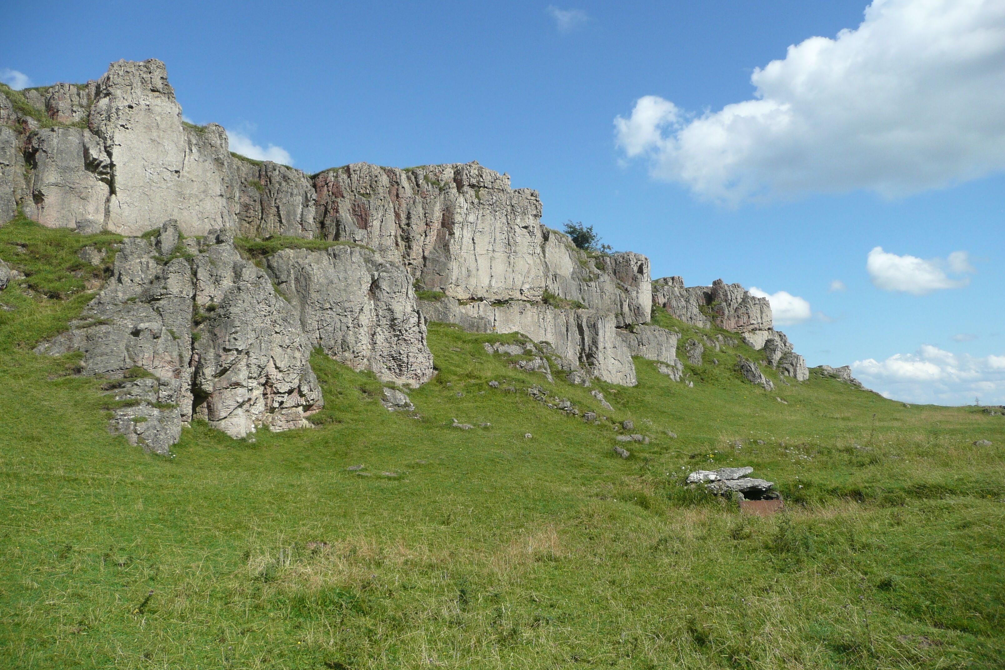 A rugged cliff with grassy slopes and a clear sky.