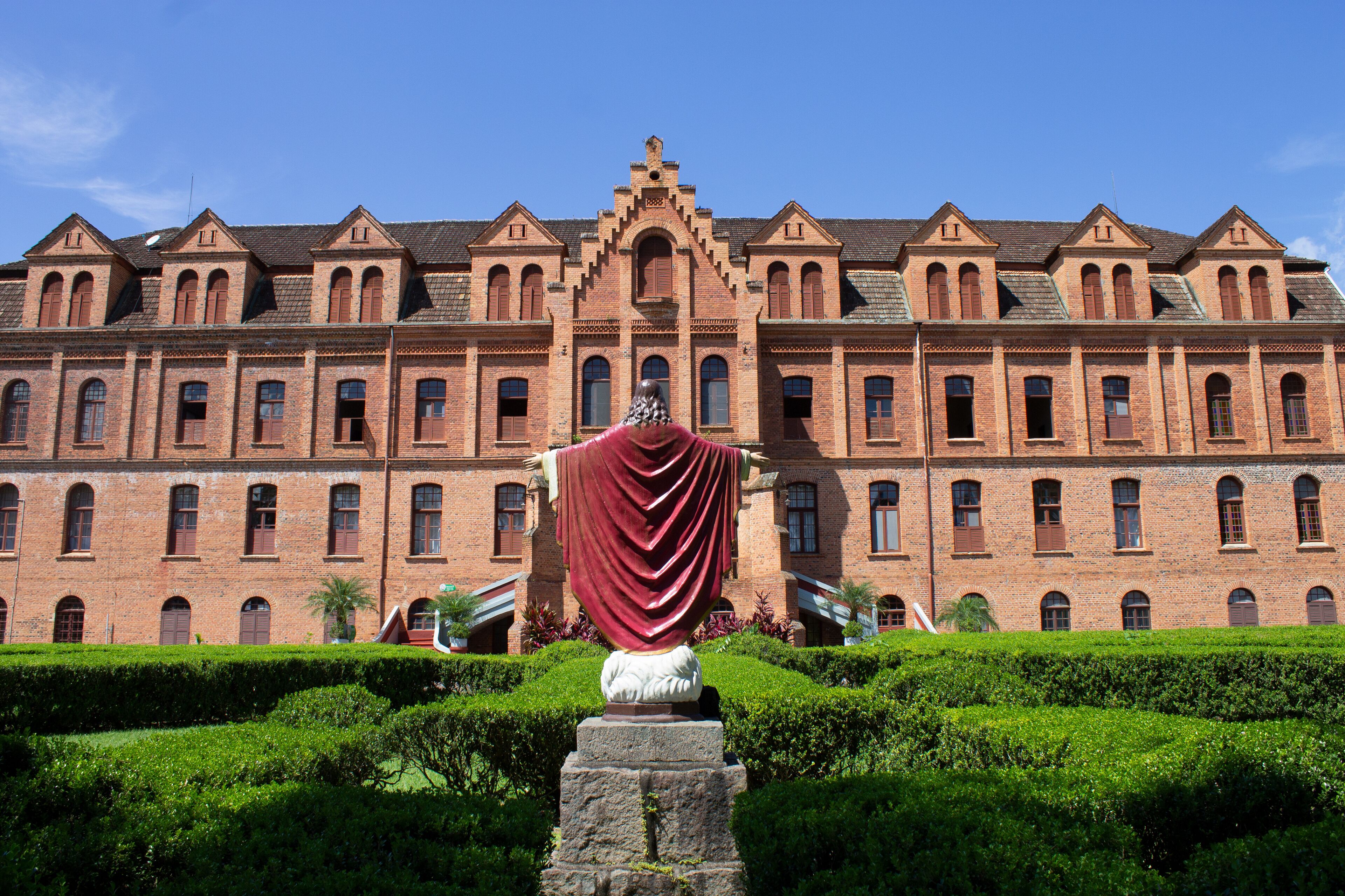 A large brick building with arched windows and a statue in front.