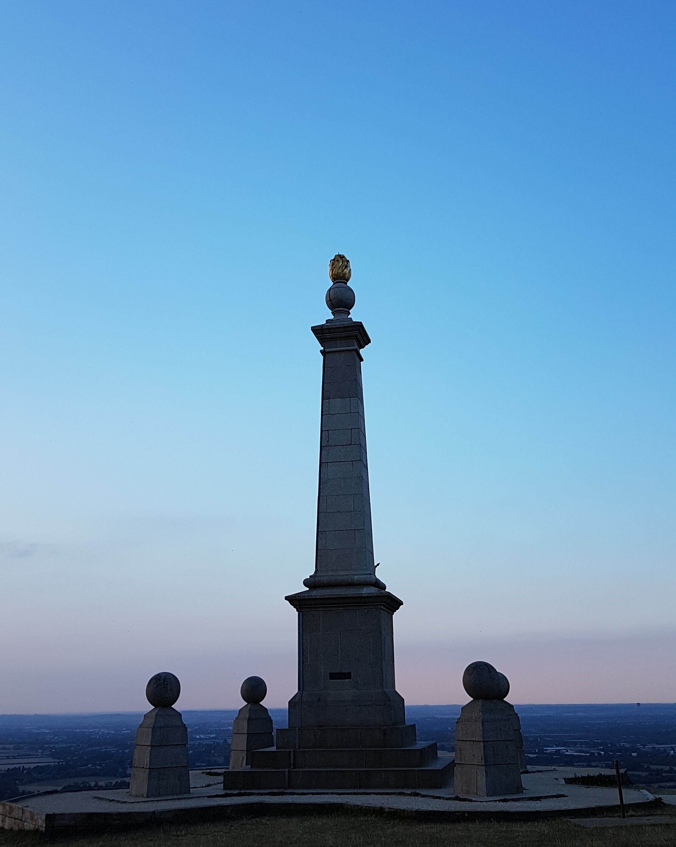 A tall monument with a spherical top and a base with four spherical decorations.